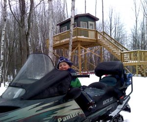 boy-sitting-on-snowmobile-in-front-of-cabin